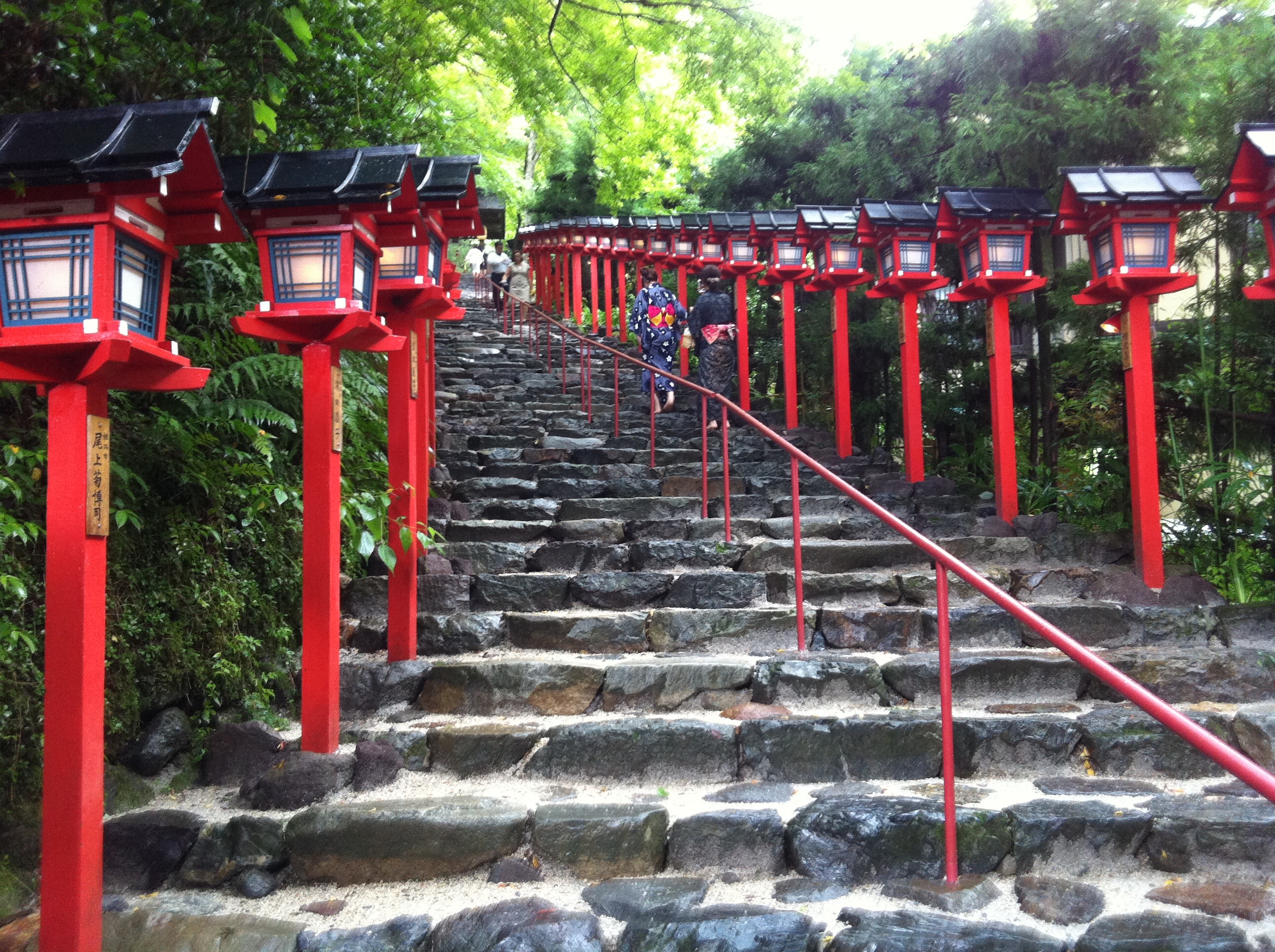 Red lantern staircase with two women in yukata ascending toward the shrine — Kyoto